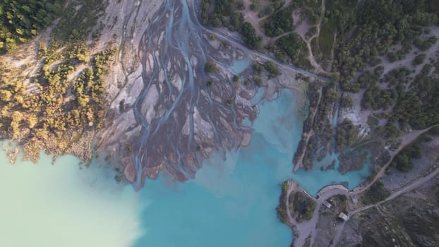 View of the mountain lake Issyk from a height. Turquoise-emerald water from the glacier. Reflection of mountains, forests and the sun on the water. The river flows into the lake. Issyk Dam. Kazakhstan