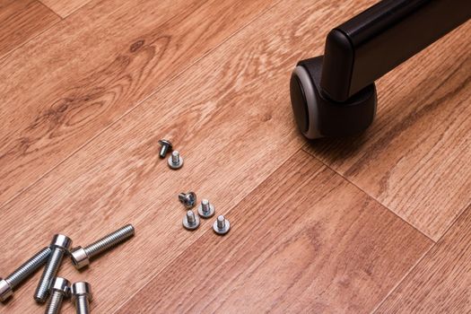 Bolts, screws and chair wheel on wooden floor close up