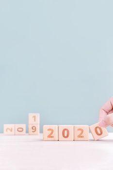 Abstract 2020 & 2019 New year countdown design concept - woman holding wood blocks cubes on wooden table and green background, close up, copy space.