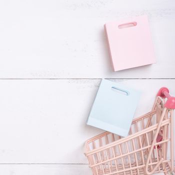 Abstract design element,annual sale,shopping season concept,mini cart with colorful paper bag on white wooden table background,top view,flat lay