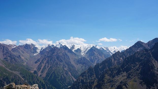 High mountains covered with snow in places. Green grass grows. Huge rocks and cliffs. In the distance, you can see peak of Talgar and Nursultan. A rocky gorge. Rowing peaks from a height. Kazakhstan