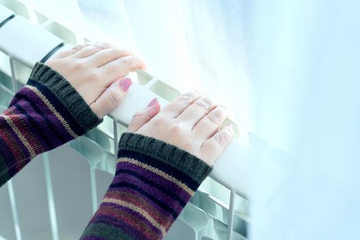 Girl warms up the frozen hands above hot radiator, close up
