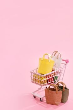 Annual sale shopping season concept - mini red shop cart trolley full of paper bag gift isolated on pale pink background, blank copy space, close up