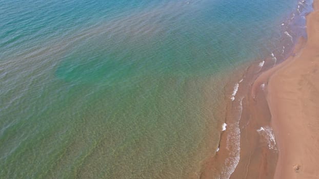 The sea touches the yellow sand with waves. Top view from a drone on a clean beach and emerald water. The sun's rays are reflected in the water. Clear blue sky. A place for relaxation. Kapchagai