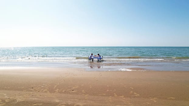 A couple in love at a table on the beach. They enjoy breakfast and the beauty of nature. Turquoise water, yellow sand and blue sky. A romantic dinner. Top view from the drone. Kapchagai, Kazakhstan.