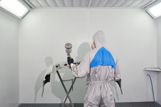 Mechanic painting bumper of a car with sprayer in painting booth