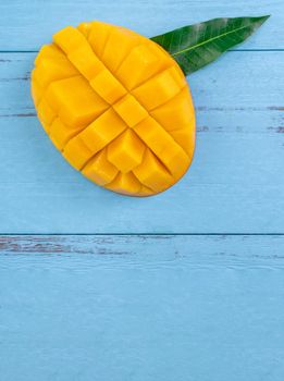 Fresh mango - beautiful chopped fruit with green leaves on bright blue timber background. Tropical fruit design concept. Flat lay. Top view. Copy space