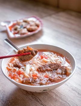 Beef noodle - Taiwan ramen meal with tomato sauce broth in bowl on bright wooden table, famous chinese style food, close up, top view, copy space