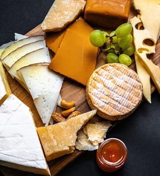 Different kinds of cheese served with grape and honey for gourmet nutrition. Organic parmesan and hard cheese set delicatessen