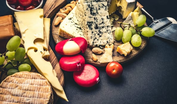 Different kinds of cheese served with grape and tomato for gourmet nutrition. Organic brie and camembert set with nuts delicatessen on black table