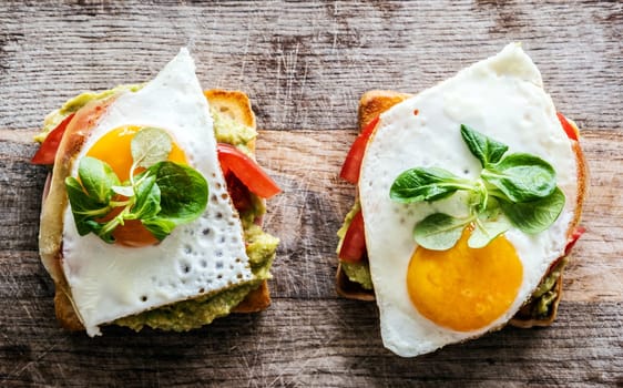 Toasted bread with egg, tomato and spinach for healthy protein breakfast on wooden table. Tasty morning sandwich with seasonal ingridients for fast diet and nutrition