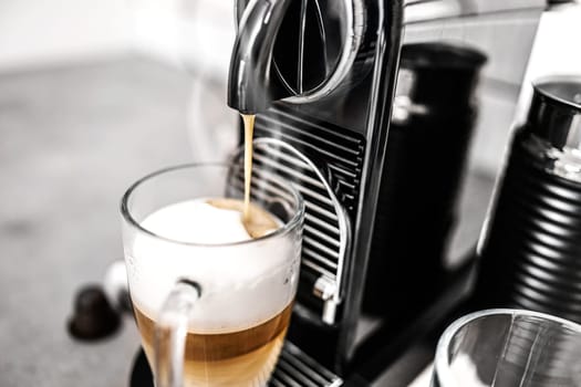 Coffee machine with capsules preparing cappuccino in transparent cup at domestic kitchen at home. Espresso caffeine beverage maker and creamy italian drink