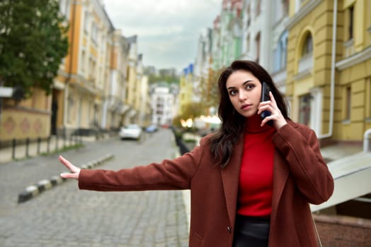 Woman on the street talking on the phone while stopping a cab.