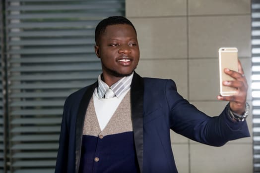 young man standing in a suit looking at cell phone while smiling.