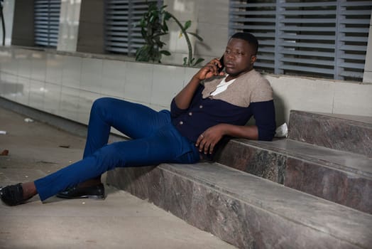 young formal formal dressed man talking on the phone while lying on a stairs outside