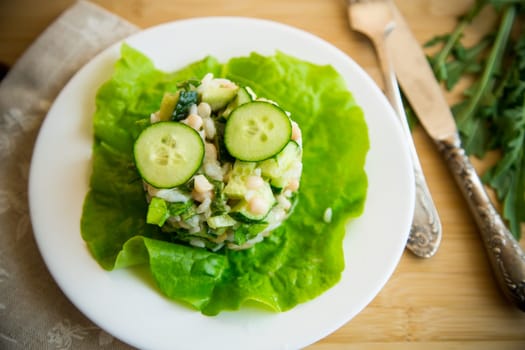 fresh summer salad with beans, rice, cucumbers and other vegetables in a plate on a wooden table.