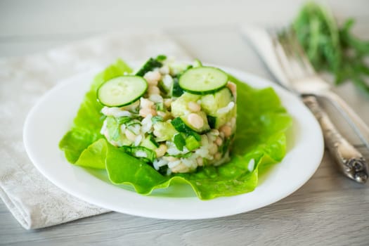 fresh summer salad with beans, rice, cucumbers and other vegetables in a plate on a wooden table.