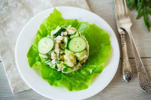 fresh summer salad with beans, rice, cucumbers and other vegetables in a plate on a wooden table.