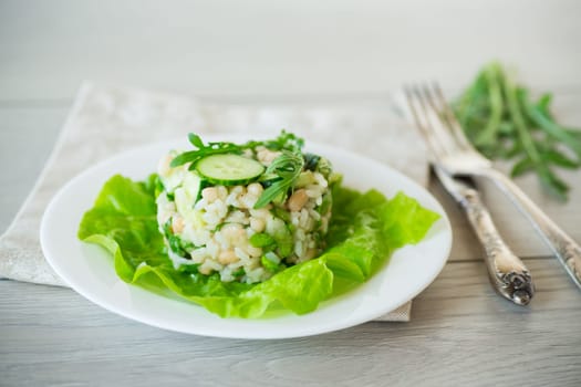fresh summer salad with beans, rice, cucumbers and other vegetables in a plate on a wooden table.