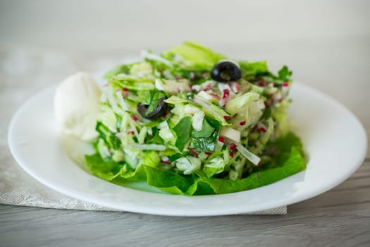 fresh summer salad with early cabbage, cucumbers, radishes and other vegetables in a plate on a wooden table.