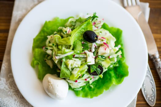 fresh summer salad with early cabbage, cucumbers, radishes and other vegetables in a plate on a wooden table.