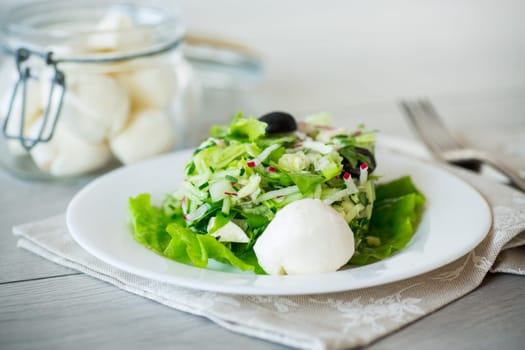 fresh summer salad with early cabbage, cucumbers, radishes and other vegetables in a plate on a wooden table.