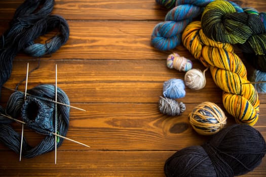 Colored threads, knitting needles and other items for hand knitting, on a dark wooden table .