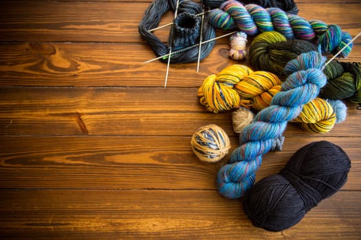 Colored threads, knitting needles and other items for hand knitting, on a dark wooden table .