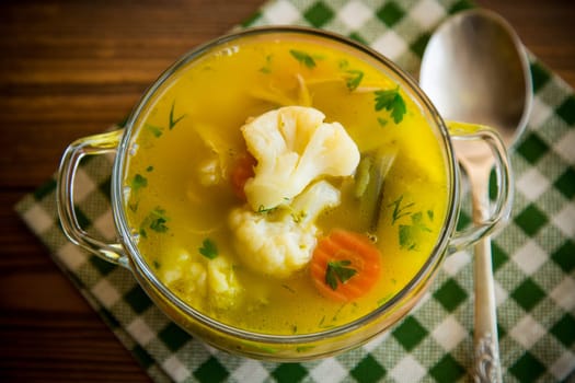 cooked chicken soup with cauliflower and vegetables in a bowl on a wooden table