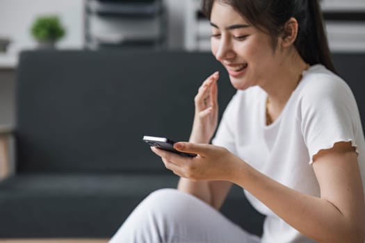 Shot of a happy young Asia woman taking selfie with her cellphone while sitting at living room...