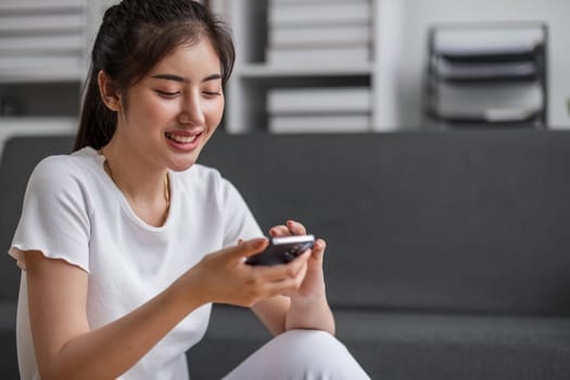 Shot of a happy young Asia woman taking selfie with her cellphone while sitting at living room...