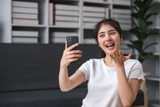 Shot of a happy young Asia woman taking selfie with her cellphone while sitting at living room...