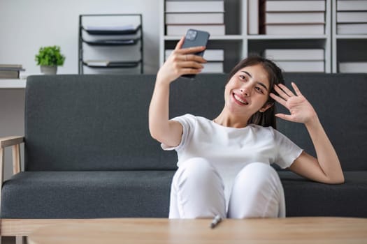 Shot of a happy young Asia woman taking selfie with her cellphone while sitting at living room...