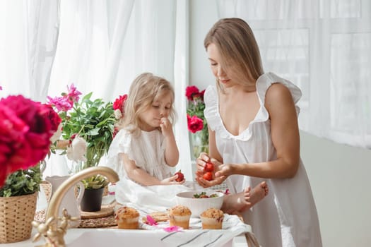 A little blonde girl with her mom on a kitchen countertop decorated with peonies. The concept of the relationship between mother and daughter. Spring atmosphere