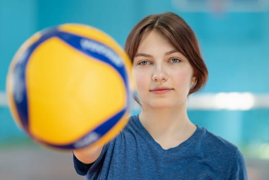 Volleyball training concept, sporty girl showing new ball to the camera
