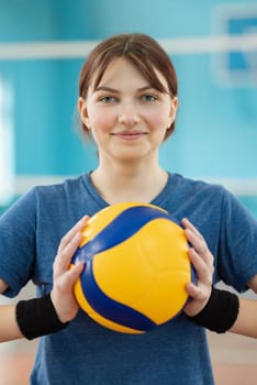 Happy female volleyball player with new professional ball in gym