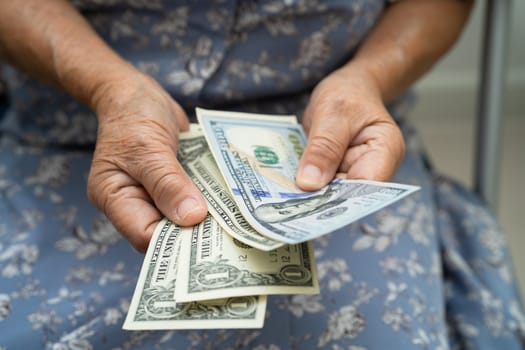 Asian senior woman holding and counting US dollar banknotes money in purse. Poverty, saving problem in retirement.