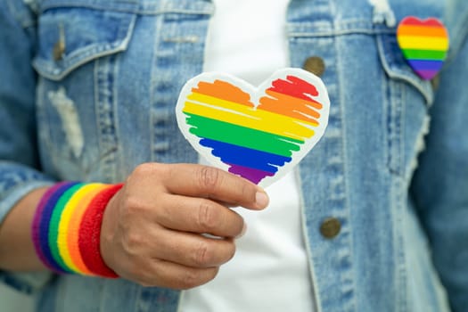 Asian lady wearing rainbow flag wristbands and hold red heart, symbol of LGBT pride month celebrate annual in June social of gay, lesbian, bisexual, transgender, human rights.