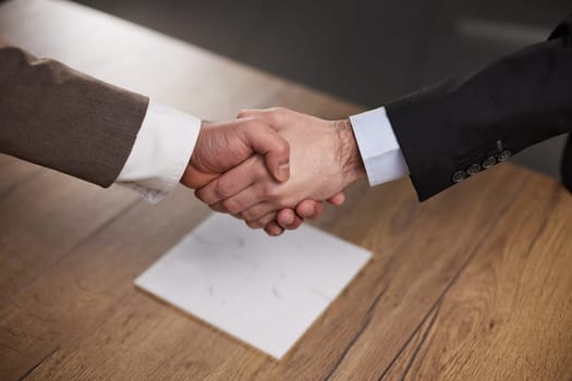 Closeup of hands of two young and successful male business people shaking hands over wooden table