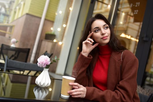 A thoughtful woman on the street, sitting outside at a table in a cafe with a cup of tea