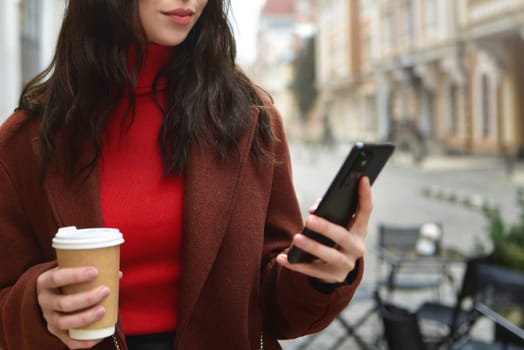 Woman use mobile phone outside holding a cup of coffee. crop photo