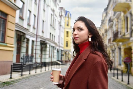 A young business woman with a cup of coffee in her hand walks down the street.