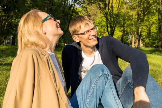 Smiling With Teeth Couple Sits On Grass In Park. Husband And Wife Enjoy Time Together, Relationship, Togetherness. Sincere Feelings. Horizontal Plane. Summer Time. High quality photo