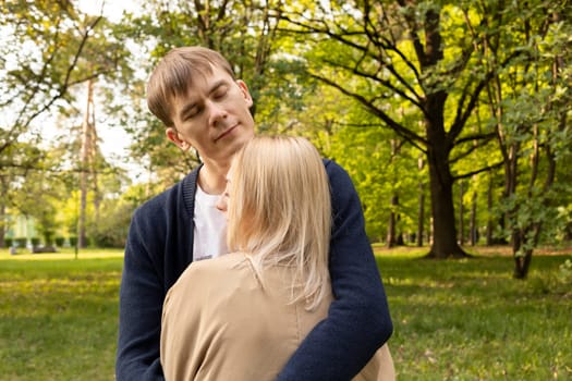 Beautiful Couple Stands Hugging With Closed Eyes In Green Park. Relationship, Togetherness. Enjoying Time Together, Harmony. Pure Feelings. Horizontal Plane Summer Time. High quality photo