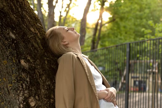 Tired White Woman Leans To Tree, Closed Her Eyes In Summer Time on Sunset. Rest And Recharge in Nature, Self Awareness, Leisure Time, Mental Health. Copy Space For Text Horizontal Plane.