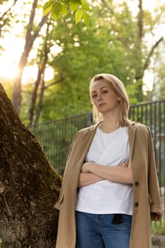 Tired White Woman Stand Near Tree With Crossed Hands, Looking At Camera on Sunset. Rest And Recharge in Nature, Self Awareness, Leisure Time, Mental Health. Copy Space For Text Vertical Plane.