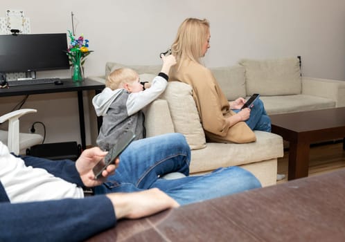 Little Boy Cuts Mother's Hair With Scissors While Parents Look, Sit At Smartphone. Deprivation, Disconnected Family, Emotionally Cold Parents, Social Issue. Horizontal Plane.