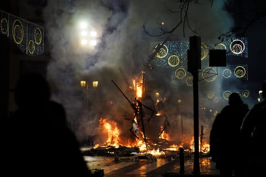 Horizontal photo of the fading Ninot doll burns on a street illuminated by lights during the Fallas celebration in Valencia, Spain