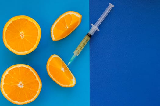 syringe is ready for mesotherapy injection. Orange in a Cut and Syringe With Vitamin C on blue background.