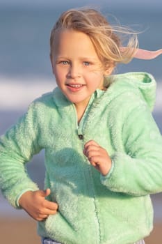 Long shot - vertical photo of a 5-year-old blonde girl with blue eyes, wearing a green jacket, is running